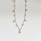 Delicate gold necklace with small teardrop and round shaped diamond pendants on a light gray background