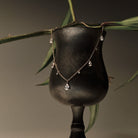 Gold Necklace with teardrop and round diamonds pendants on a black stand with green leaves in the background.