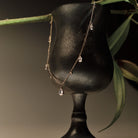 Gold Necklace with teardrop and round diamonds pendants on a black stand with green leaves in the background.