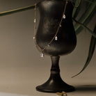 Gold Necklace with teardrop and round diamonds pendants on a black stand with green leaves in the background.