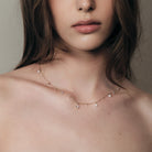 Close-up of a woman wearing a delicate teardrop diamonds necklace with a neutral background.