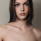 Woman wearing a delicate teardrop diamonds necklace against a neutral background.