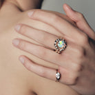Close-up of a hand wearing a marquise diamond signet ring, and a band with an australian opal ring on a neutral background.