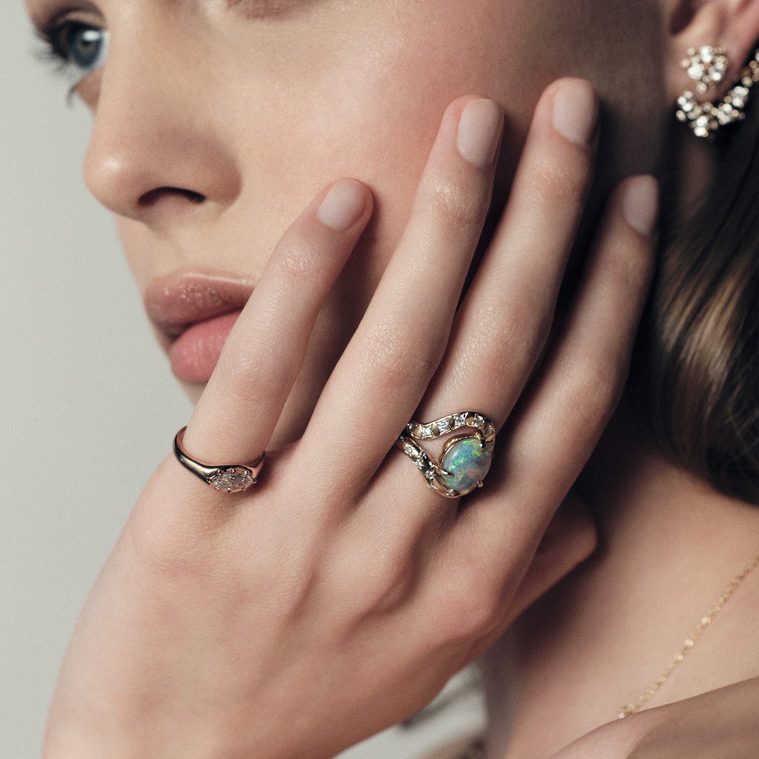 Close-up of a hand wearing a marquise diamond signet ring, and a band with an australian opal ring on a neutral background.