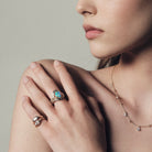Close-up of a woman's hand wearing an opal ring with a neutral background.