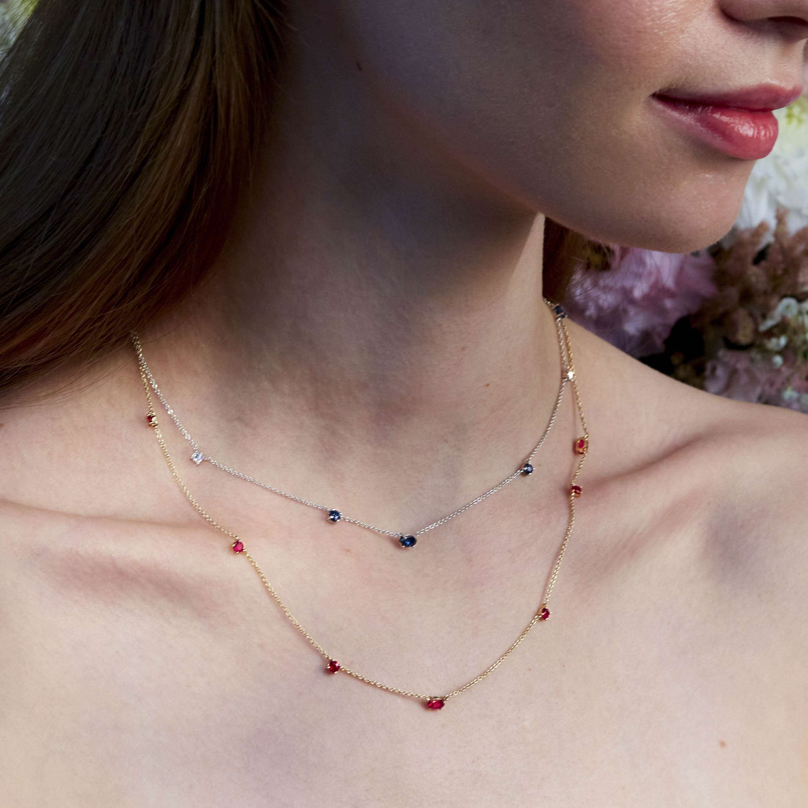 A person wearing a delicate gold chainlink necklace adorned with natural rubies.