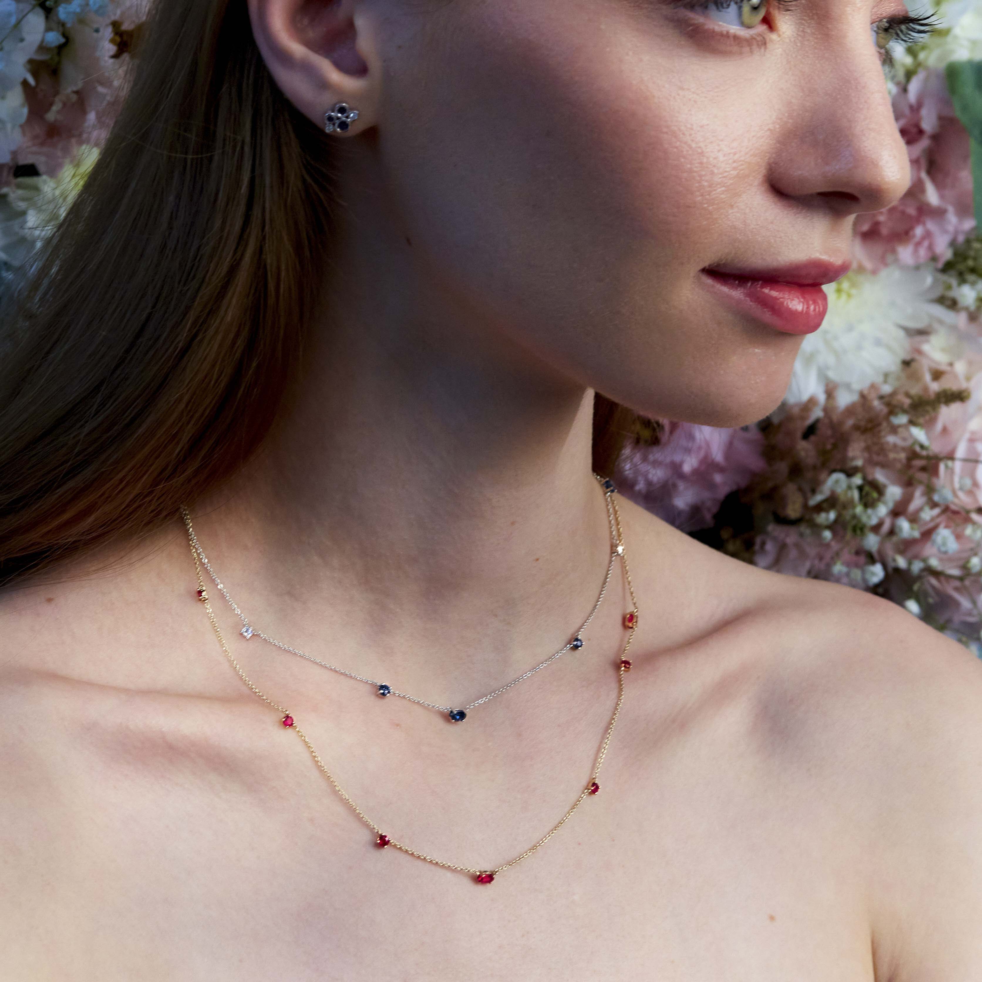 A woman wearing a delicate gold chainlink necklace adorned with natural rubies.
