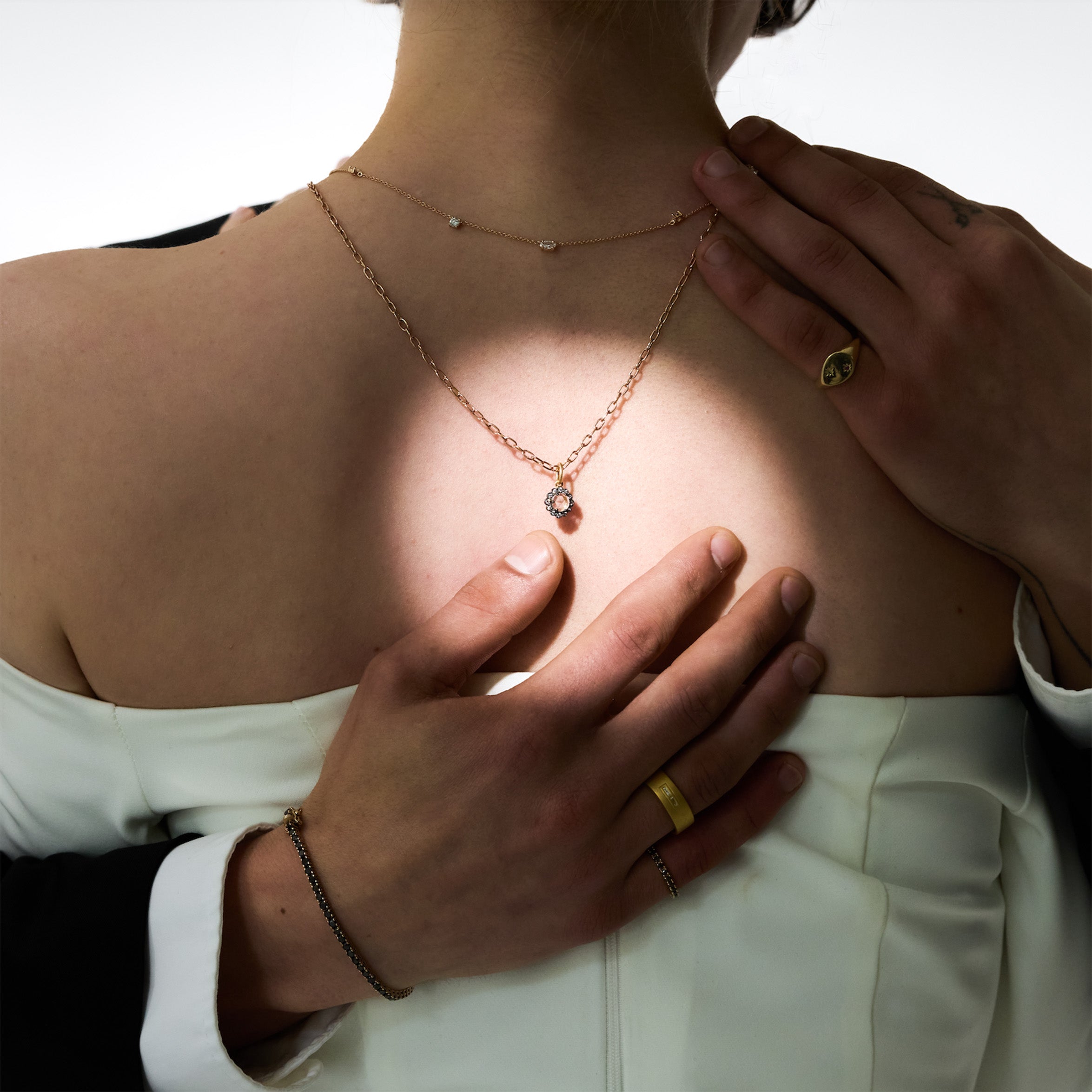 Two hands holding hugging a woman, wearing gold wedding rings, black diamonds tennis bracelet and ring, on a neutral background