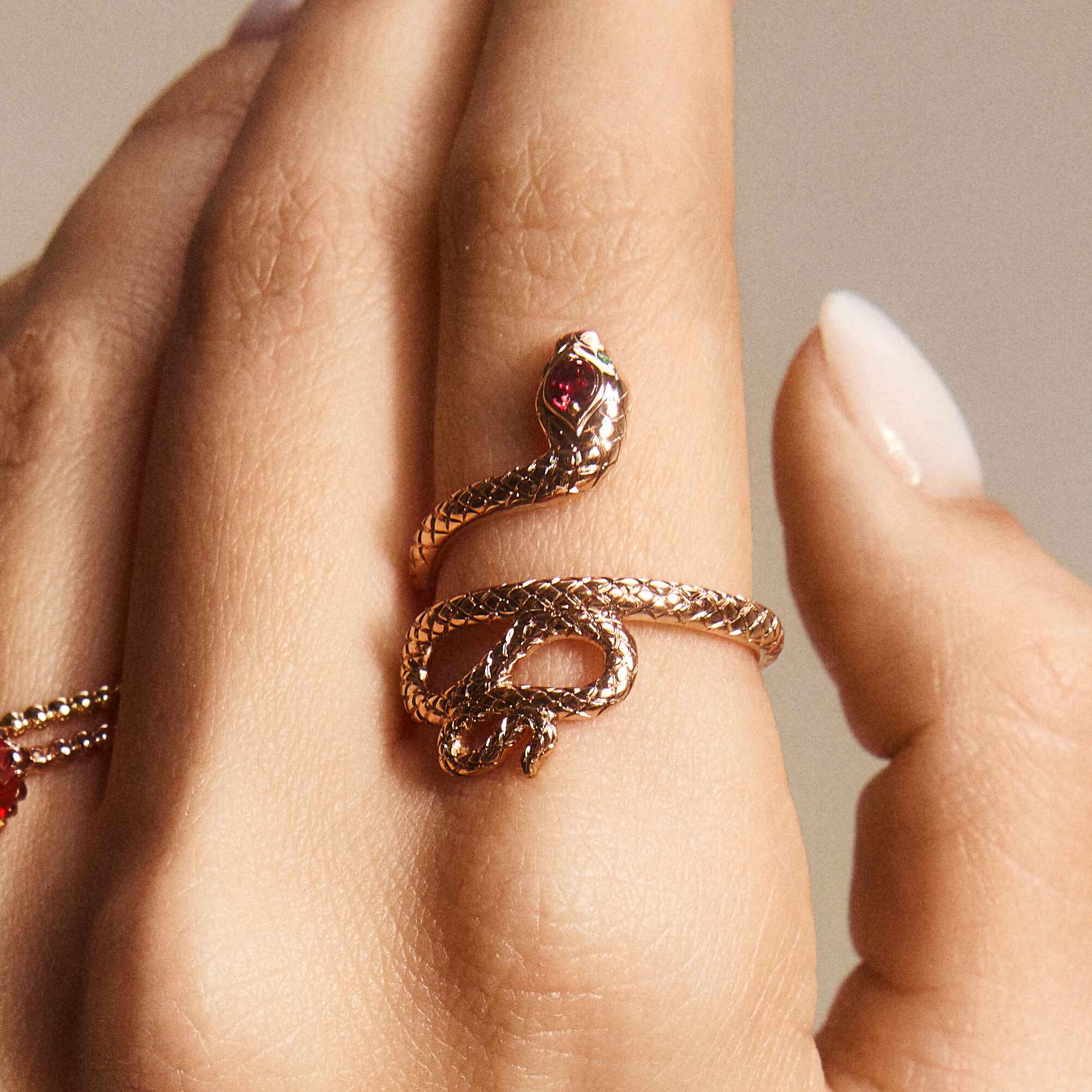 A snake ring with a red sapphire headstone and emerald eyes, displayed on a person's hand.