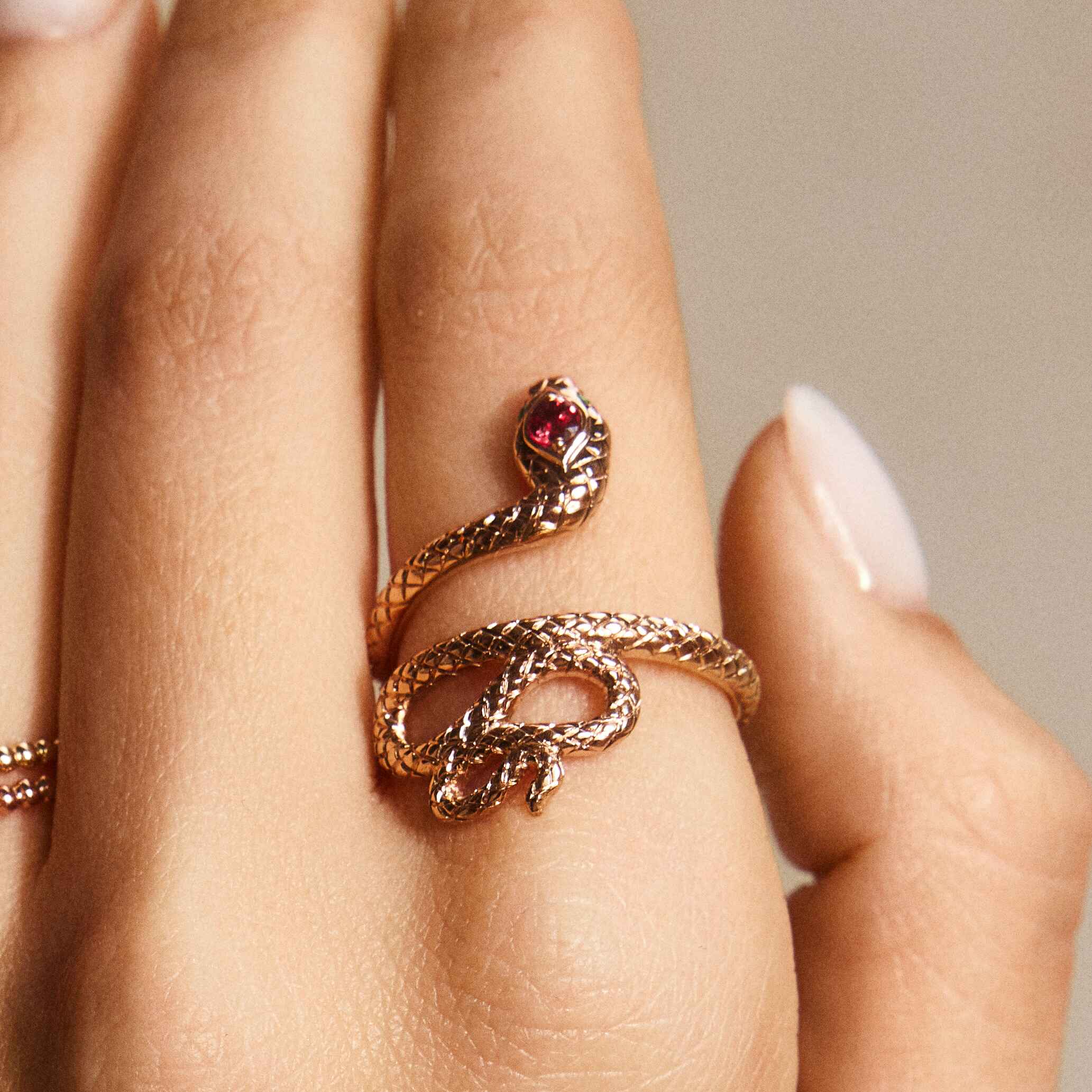A snake ring with a red sapphire headstone and emerald eyes, displayed on a person's hand.