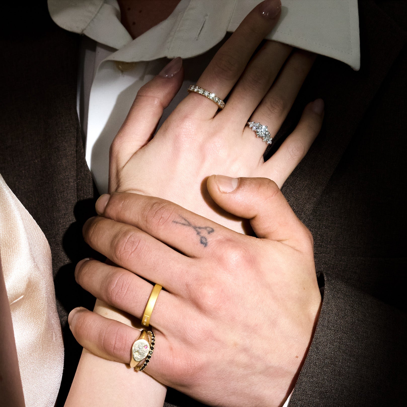 Close-up of two hands holding each other, wearing rings with visible jewelry.
