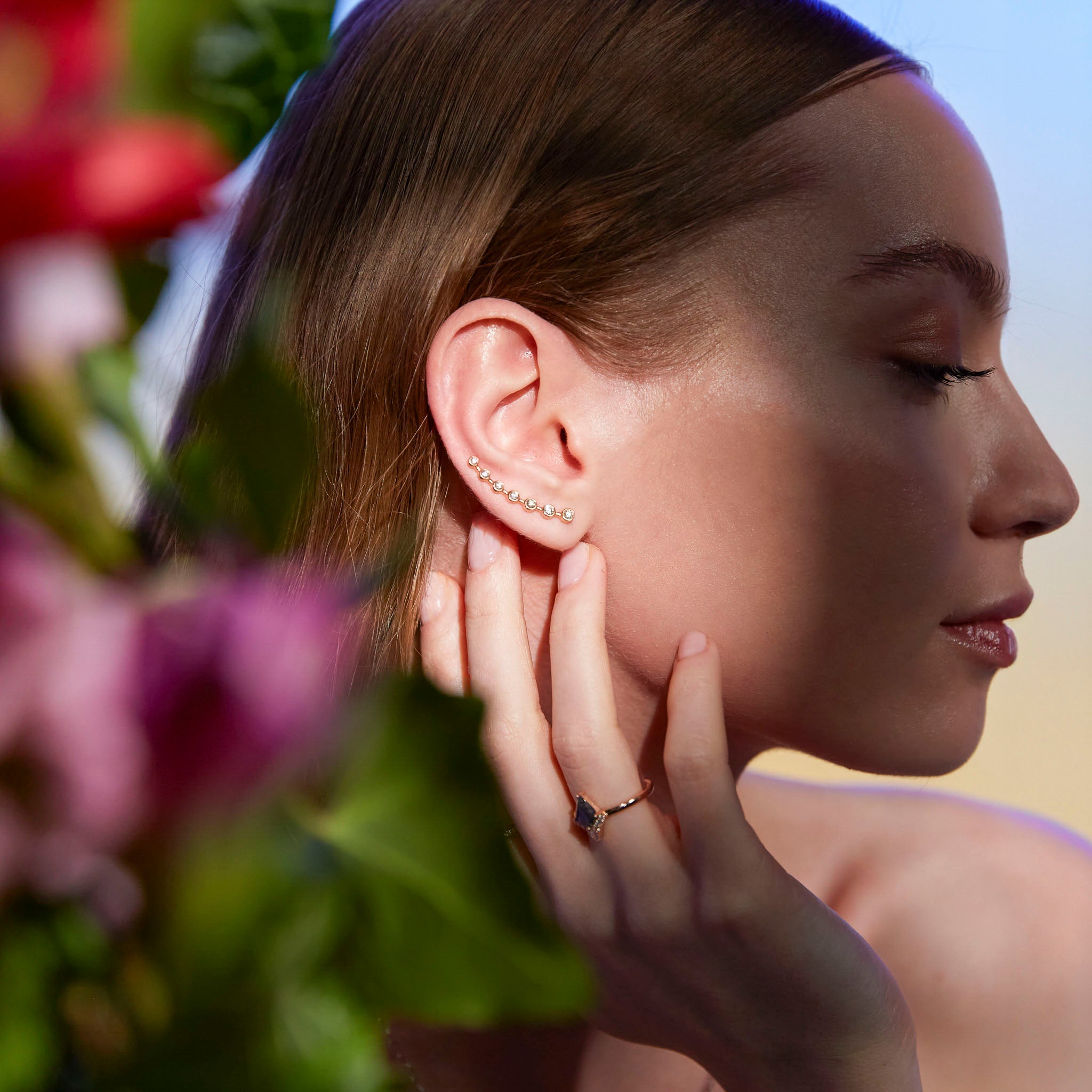 A close-up image of a woman's ear wearing a gold ear-crawler earring adorned with white diamonds.