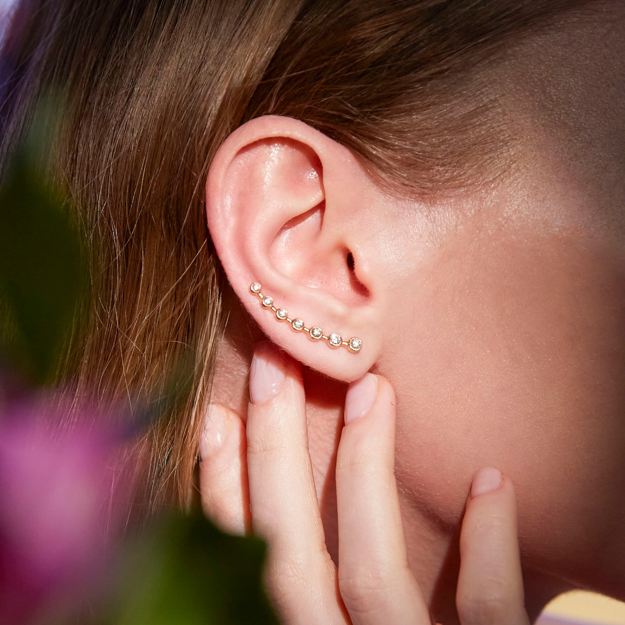 A close-up image of a woman's ear wearing a gold ear-crawler earring adorned with white diamonds.