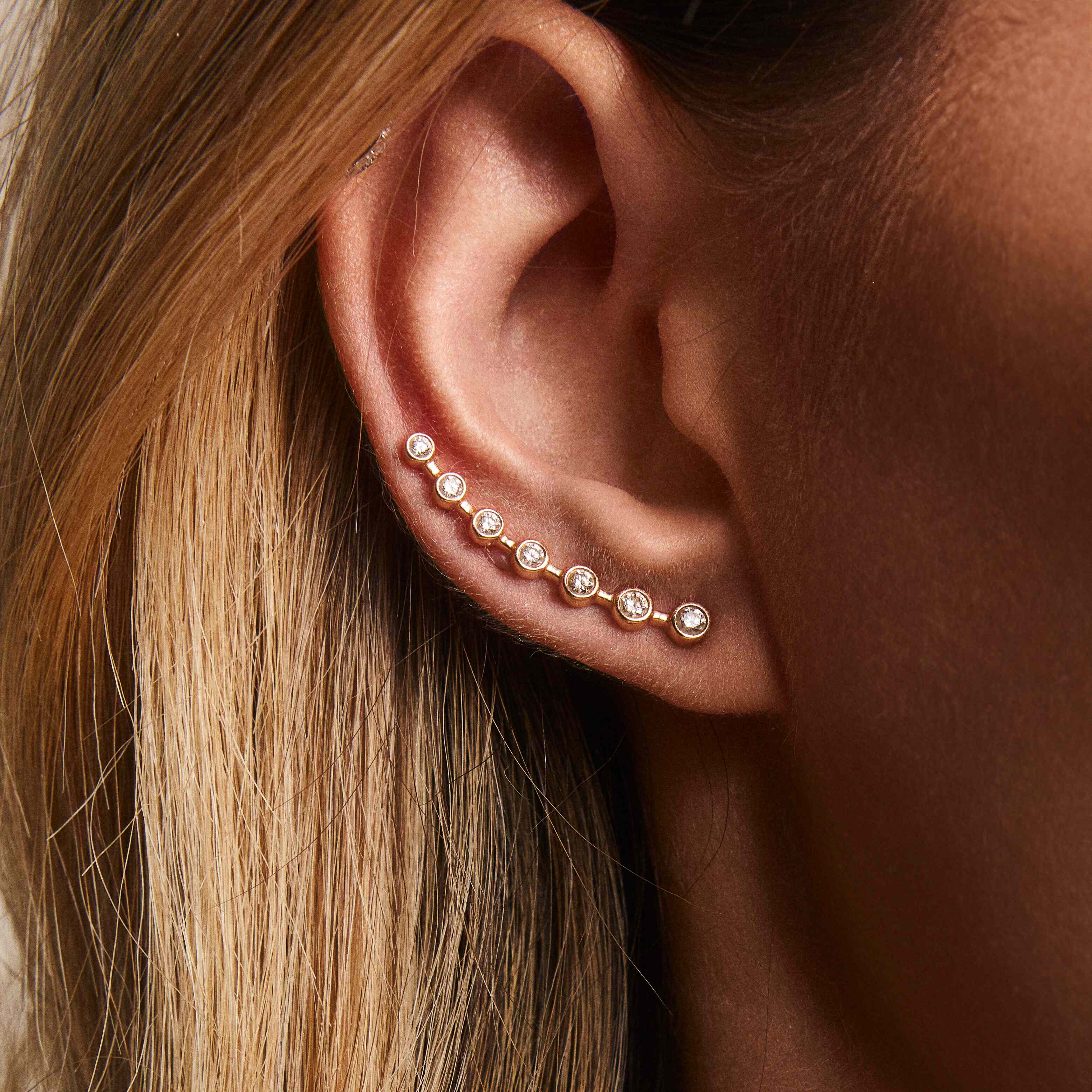 A close-up image of a woman's ear wearing a gold ear-crawler earring adorned with white diamonds.