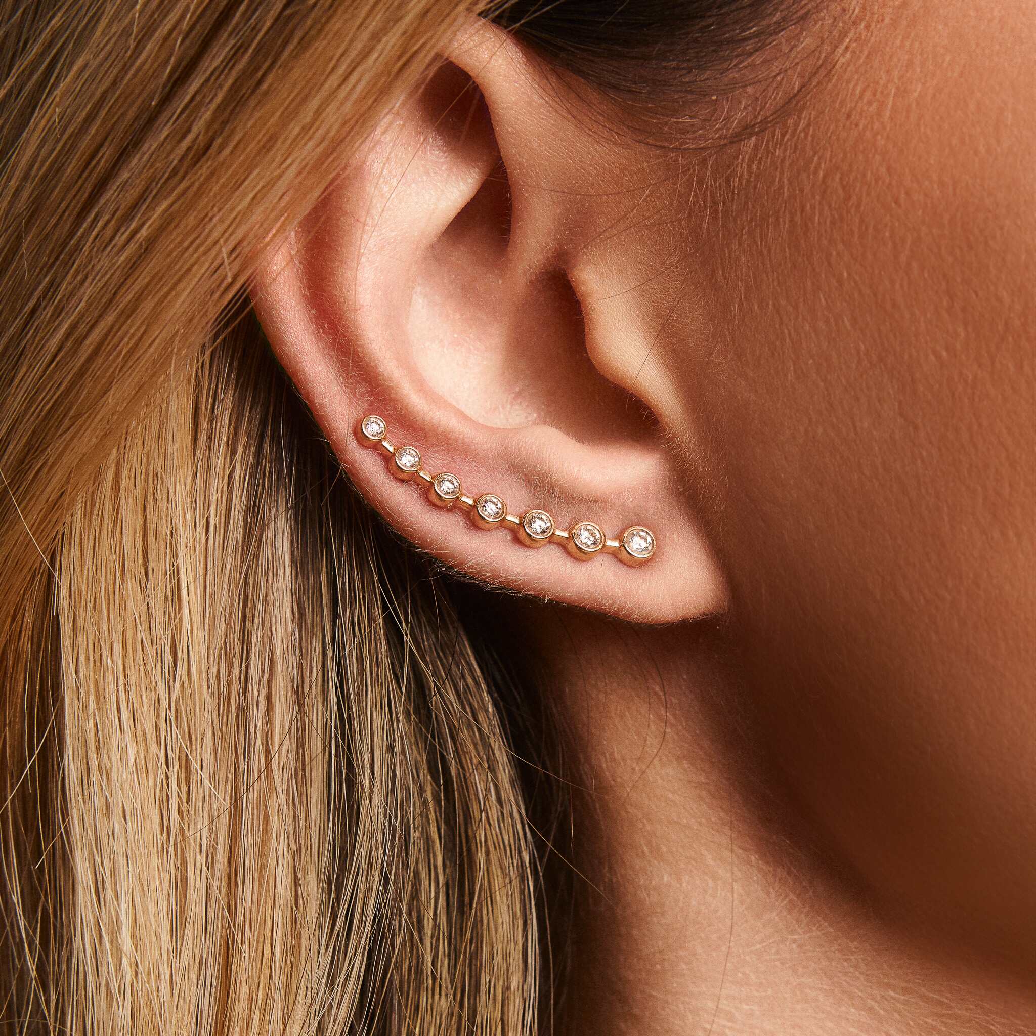 A close-up image of a woman's ear wearing a gold ear-crawler earring adorned with white diamonds.