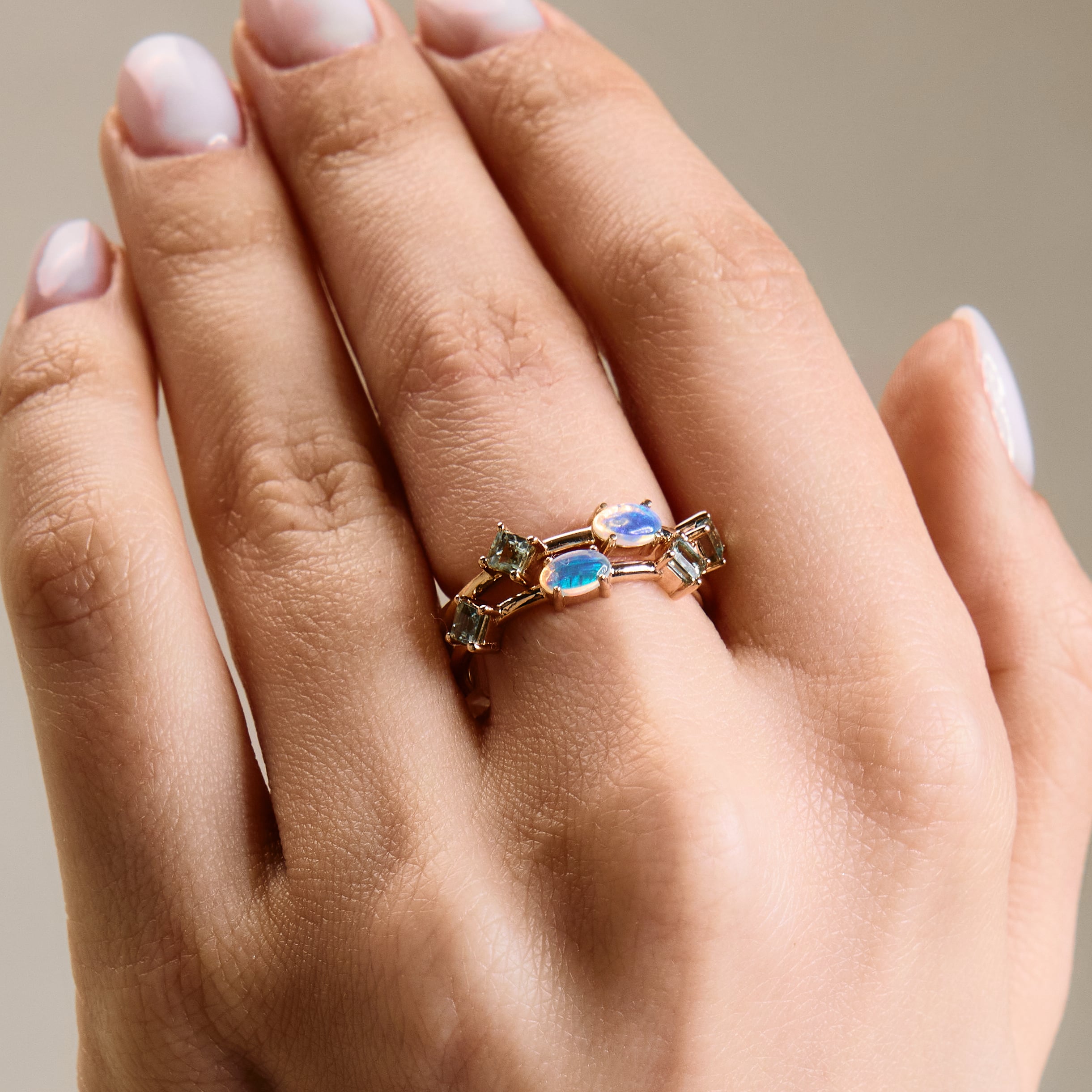 A person's hand showcasing two stackable rings with Australian Opal and green sapphires on each finger.