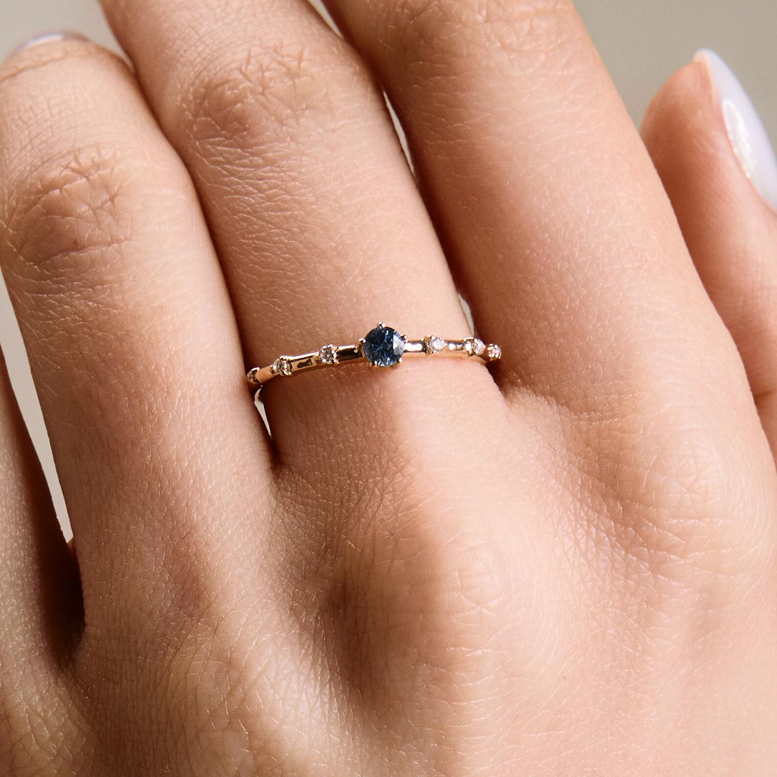 A gold band ring featuring a central sapphire with smaller diamond accents around it, presented on an a hand.