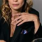 Woman wearing jewelry including a necklace, ring, and earrings with a dark blazer and colorful pocket square.