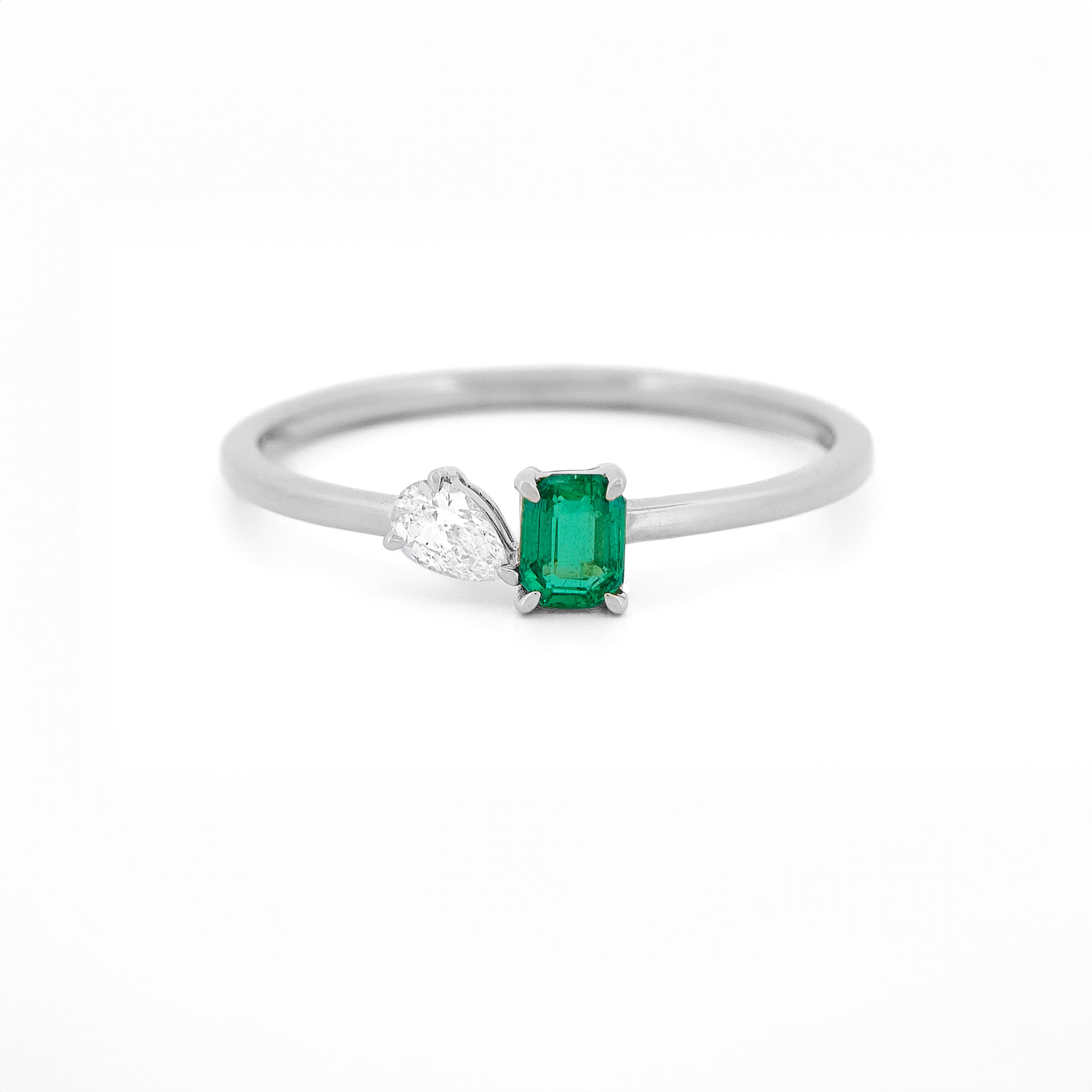 White gold toi et moi ring with an emerald and a diamonds on a white background