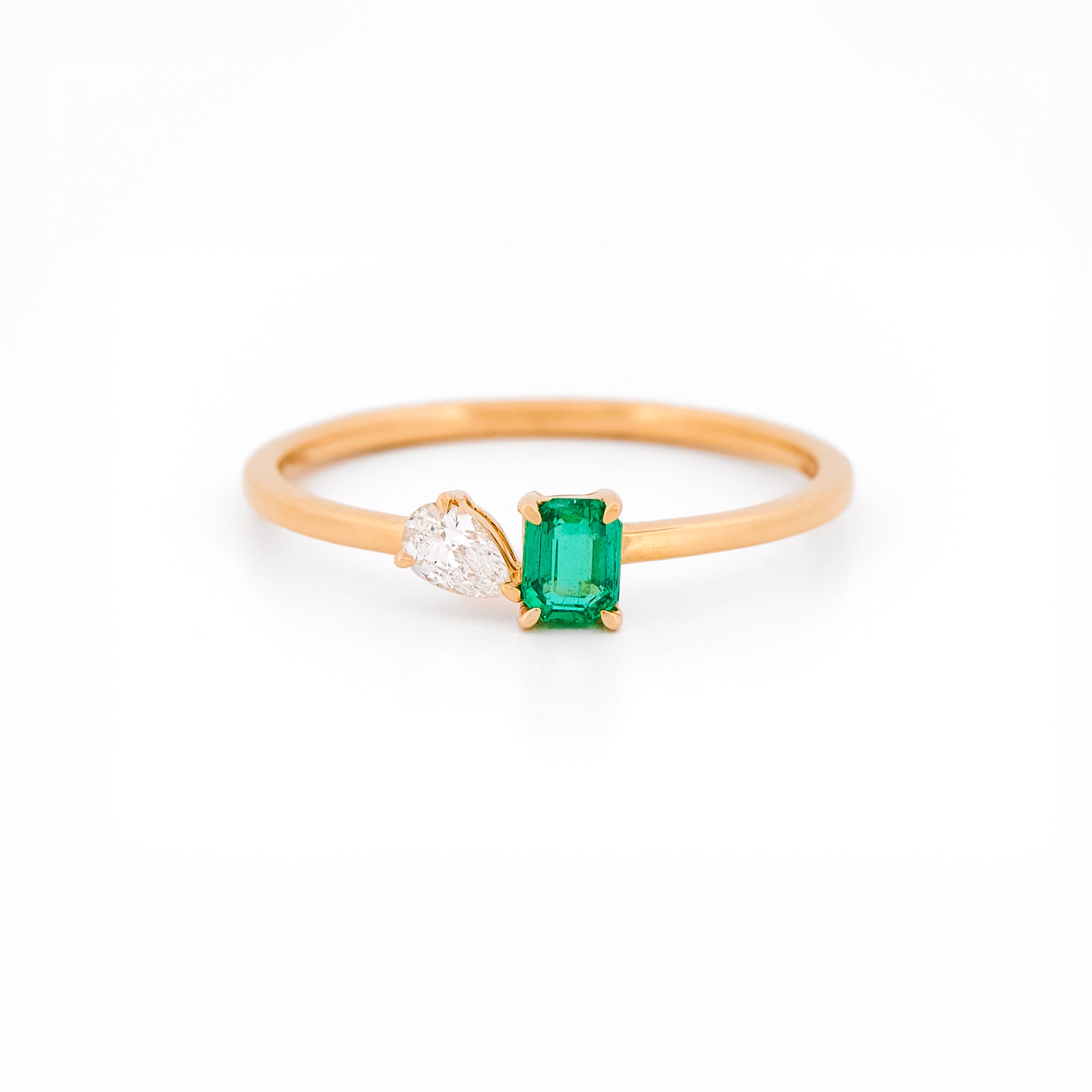 Yellow gold toi et moi ring with an emerald and a diamonds on a white background