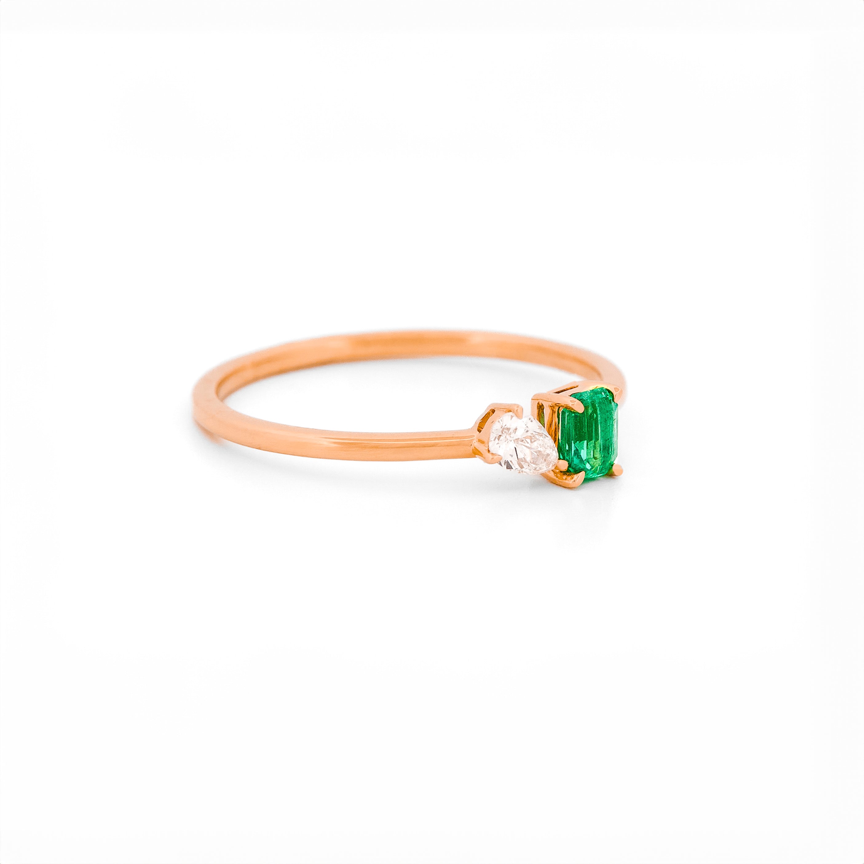 Rose gold toi et moi ring with an emerald and a diamonds on a white background