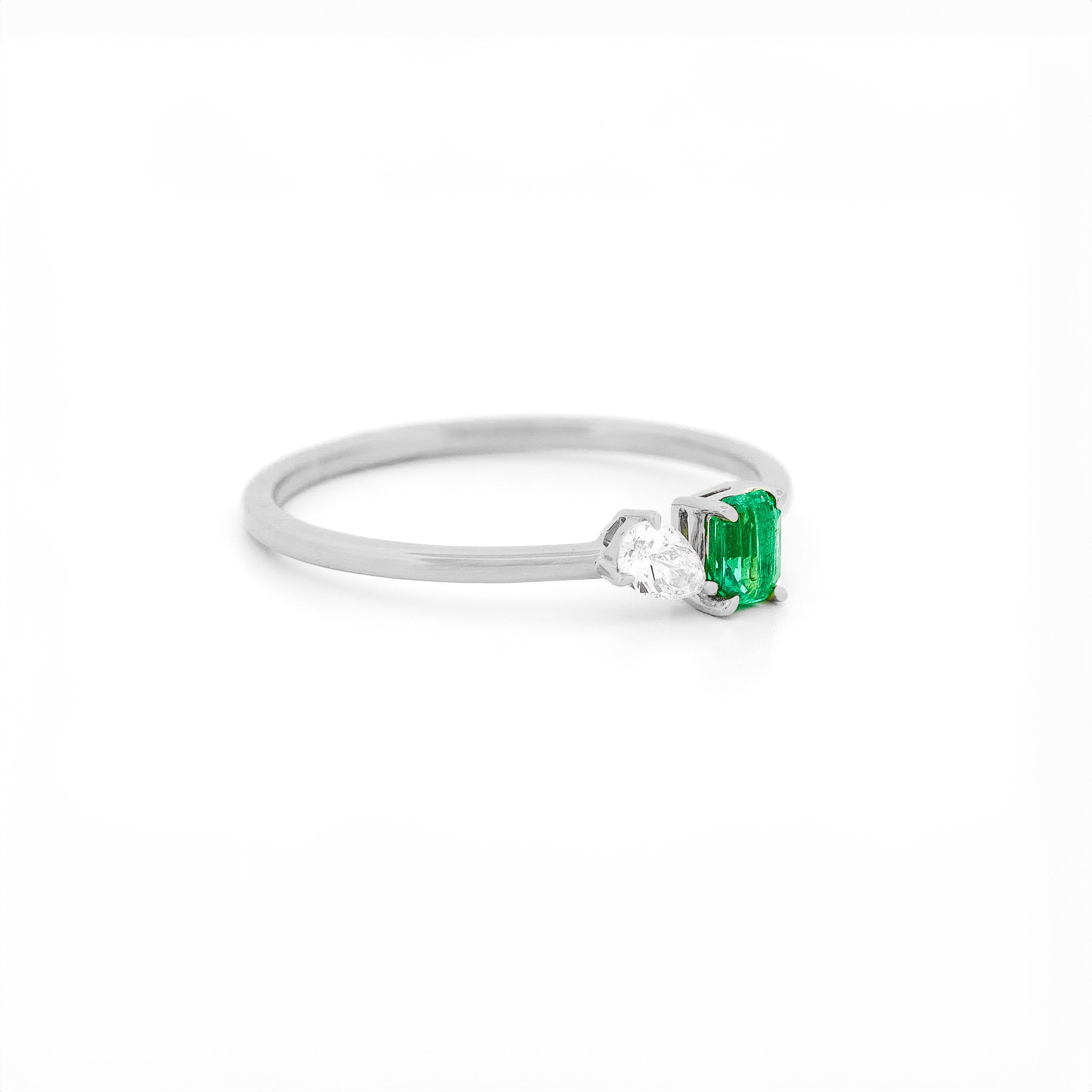 White gold toi et moi ring with an emerald and a diamonds on a white background