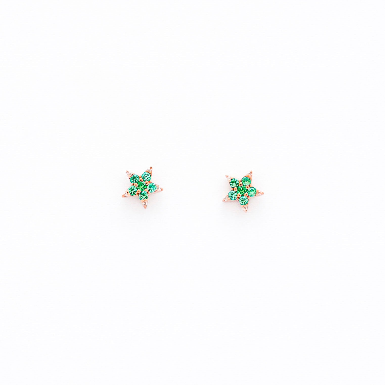 A pair of star-shaped stud earrings crafted from 14k gold, featuring round emeralds and diamonds.