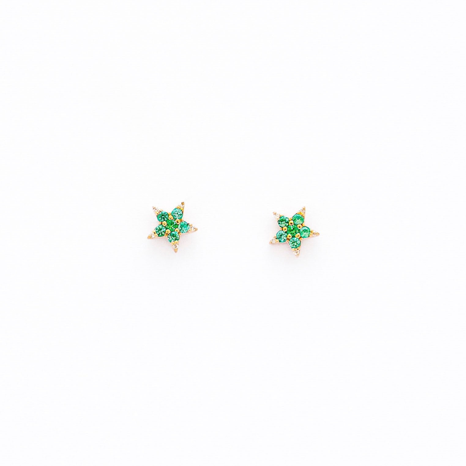 A pair of star-shaped stud earrings crafted from 14k gold, featuring round emeralds and diamonds.