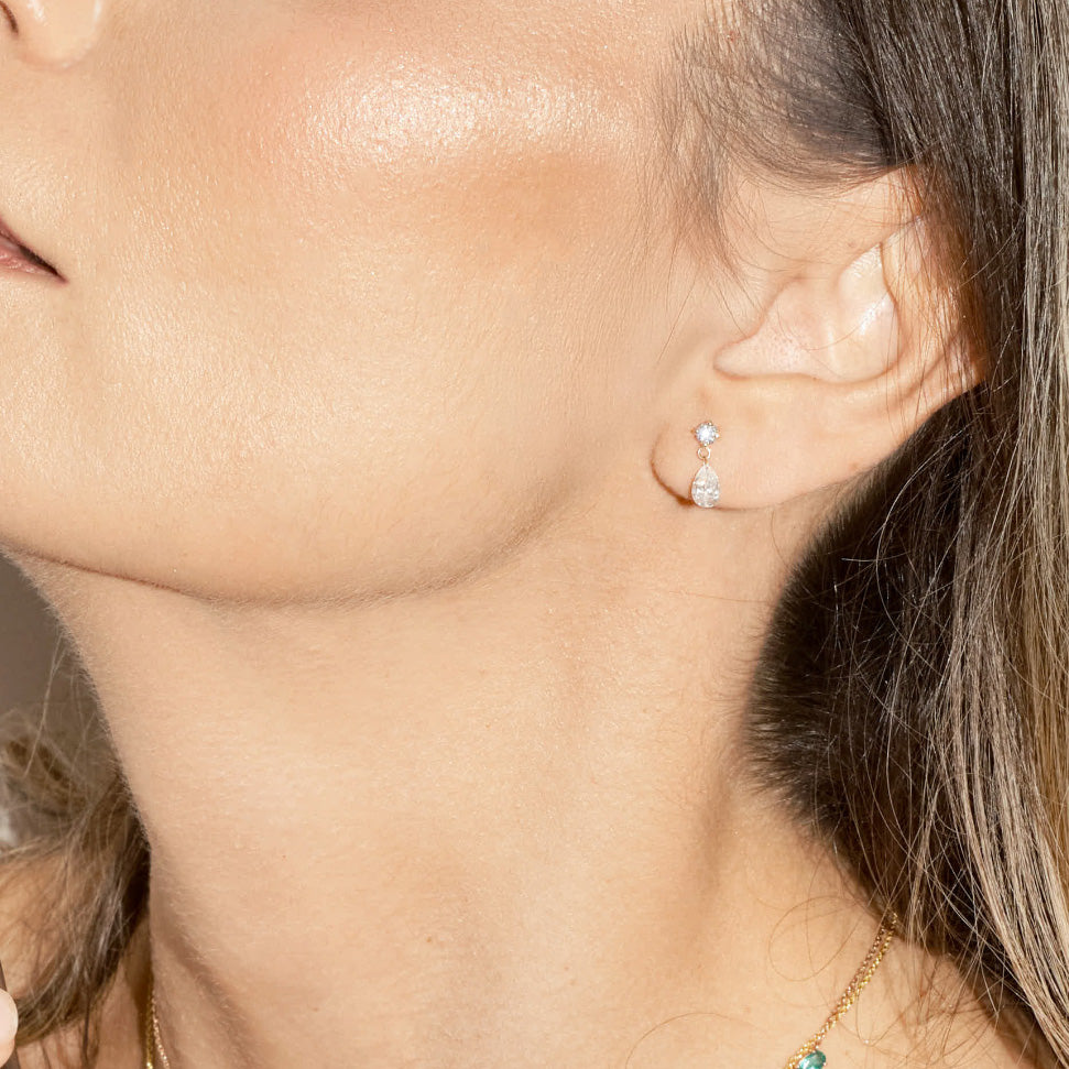 Close-up of a person wearing a teardrop diamond stud earring.