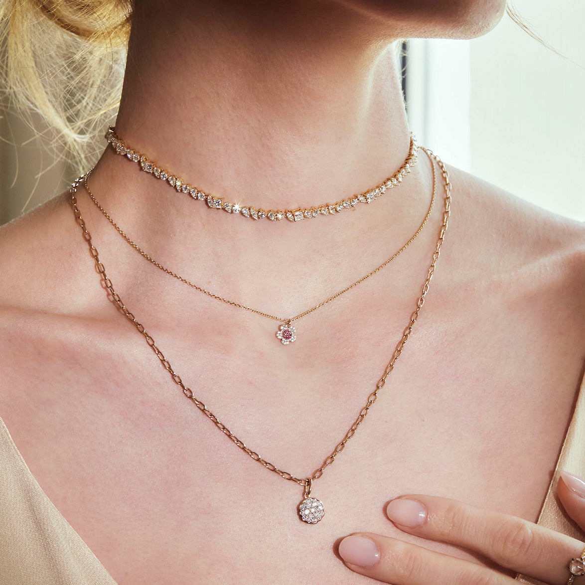 Close-up of a person wearing multiple diamonds necklaces - tennis necklace, cherry blossom flower necklace, daisy diamond pendant, on a blurred background