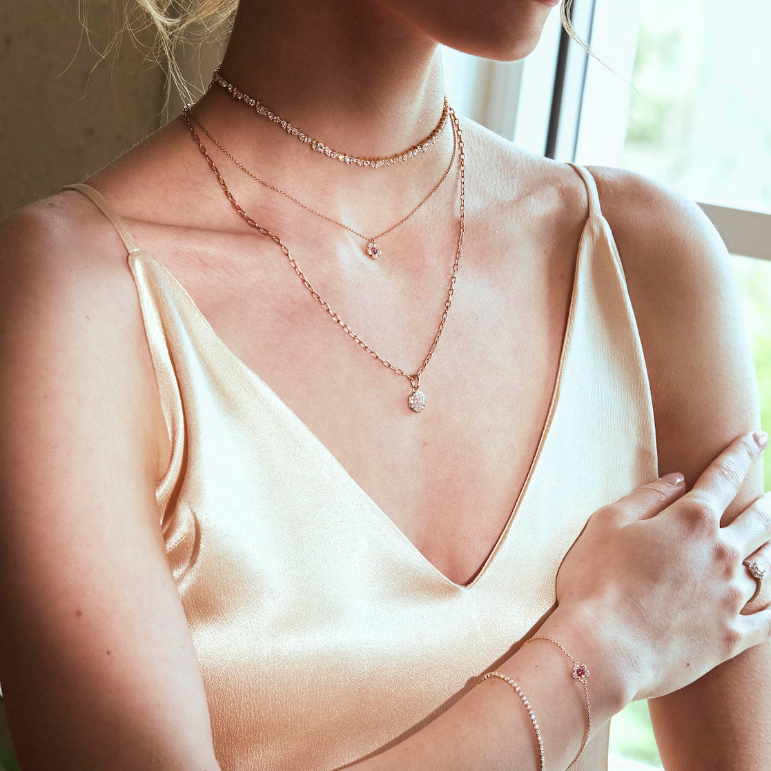 Woman wearing a beige slip dress with layered diamonds necklaces and bracelets, soft and elegant.