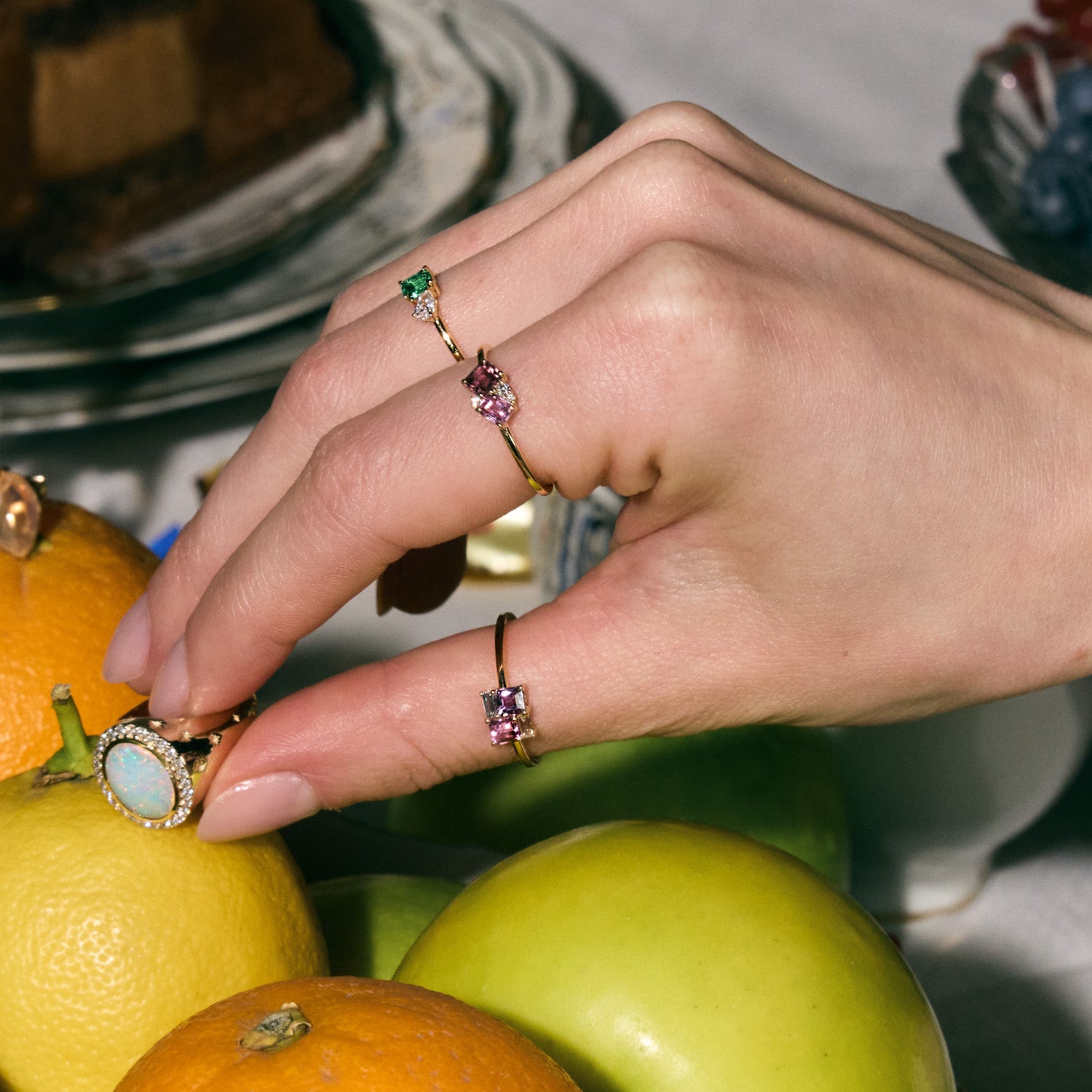 Hand with multicolored gemstone rings on a background of fruits