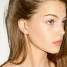 Close-up of a woman wearing small earrings, a floating diamond dot, and a a flash diamonds stud, with a plain background