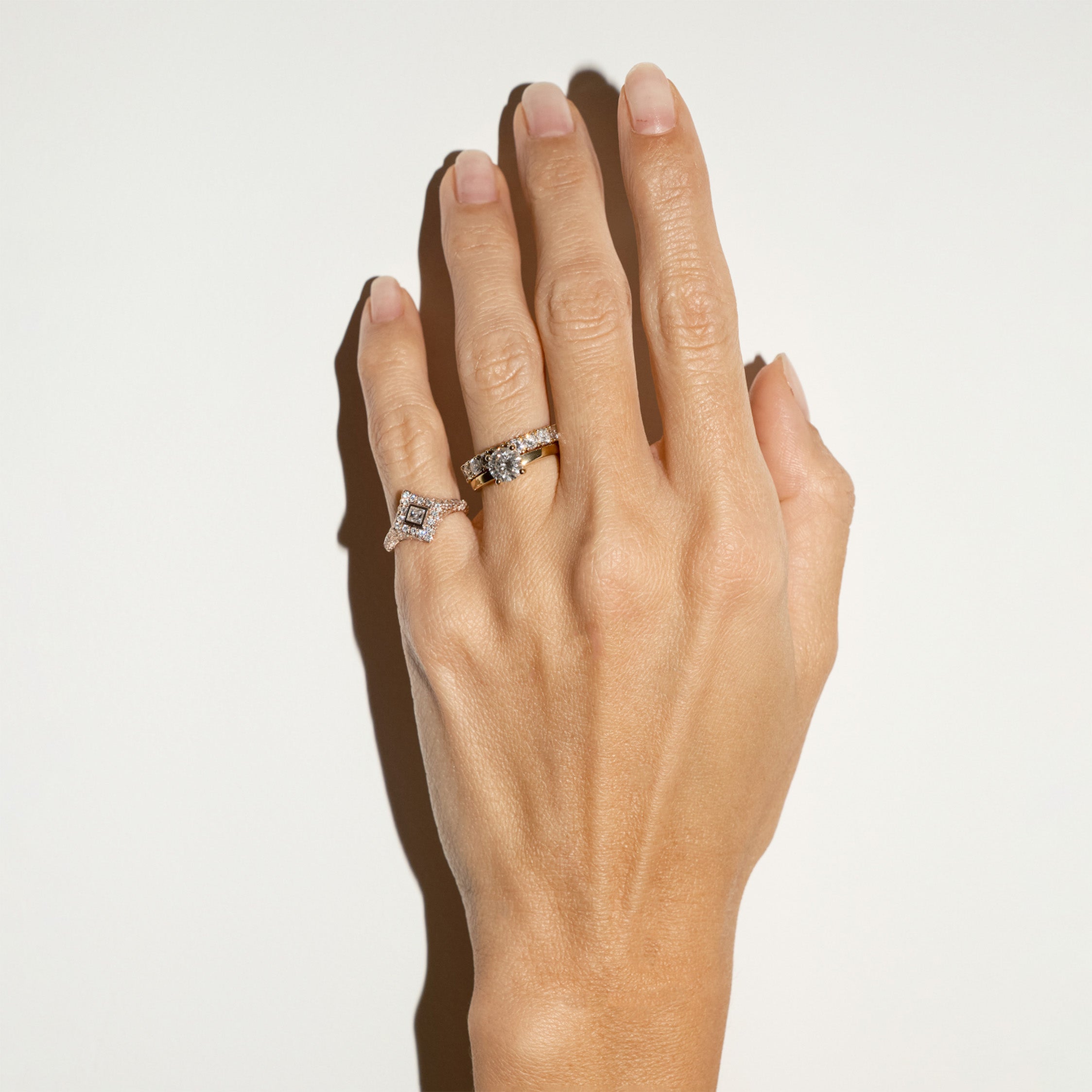 Hand wearing gold and diamond rings on a light background