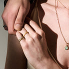 Close-up of holding hands with gold rings and a necklace against a neutral background