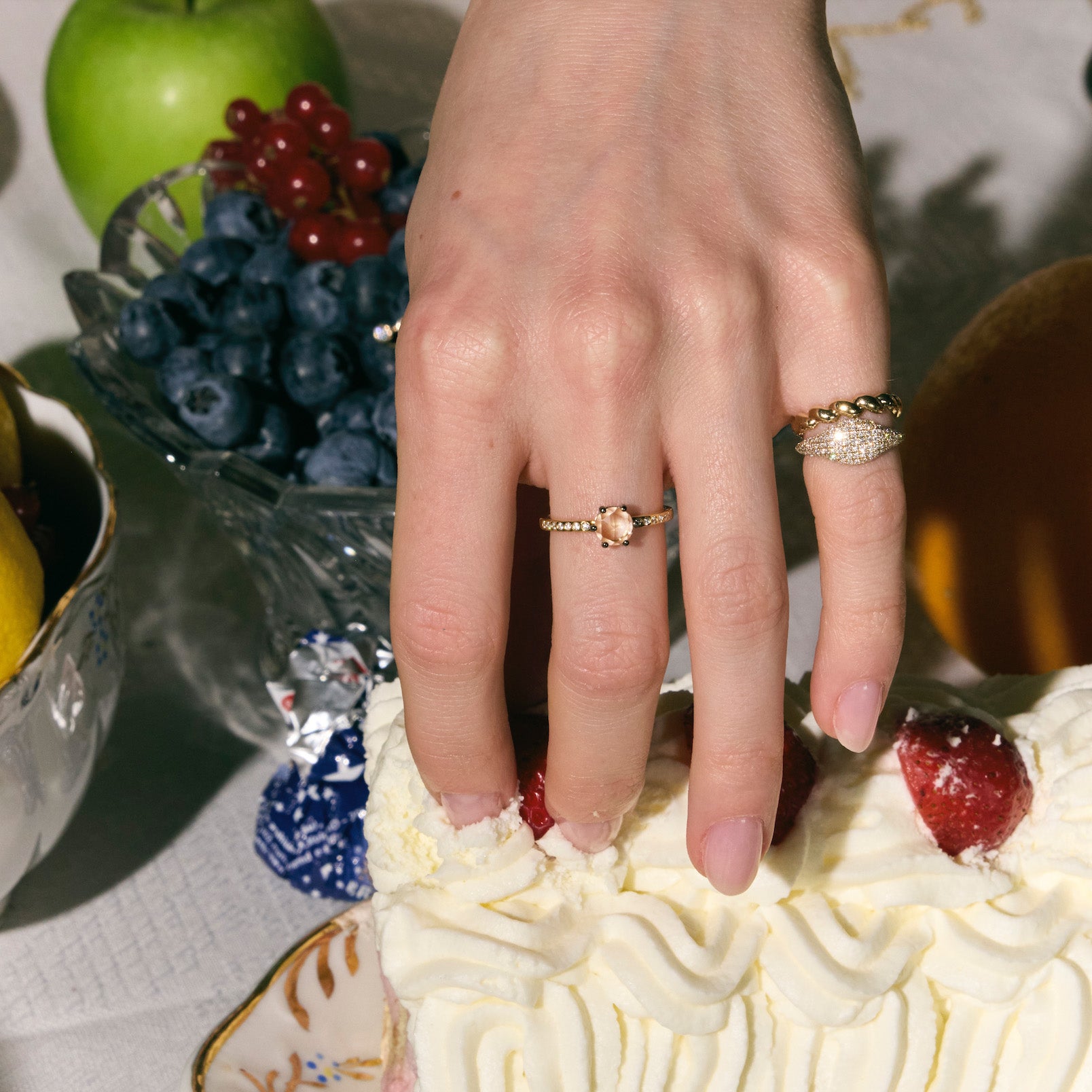 Close-up of a hand wearing three rings, one with rose-cut diamond, a pinky paved diamonds ring and a twisted band, on a dessert background