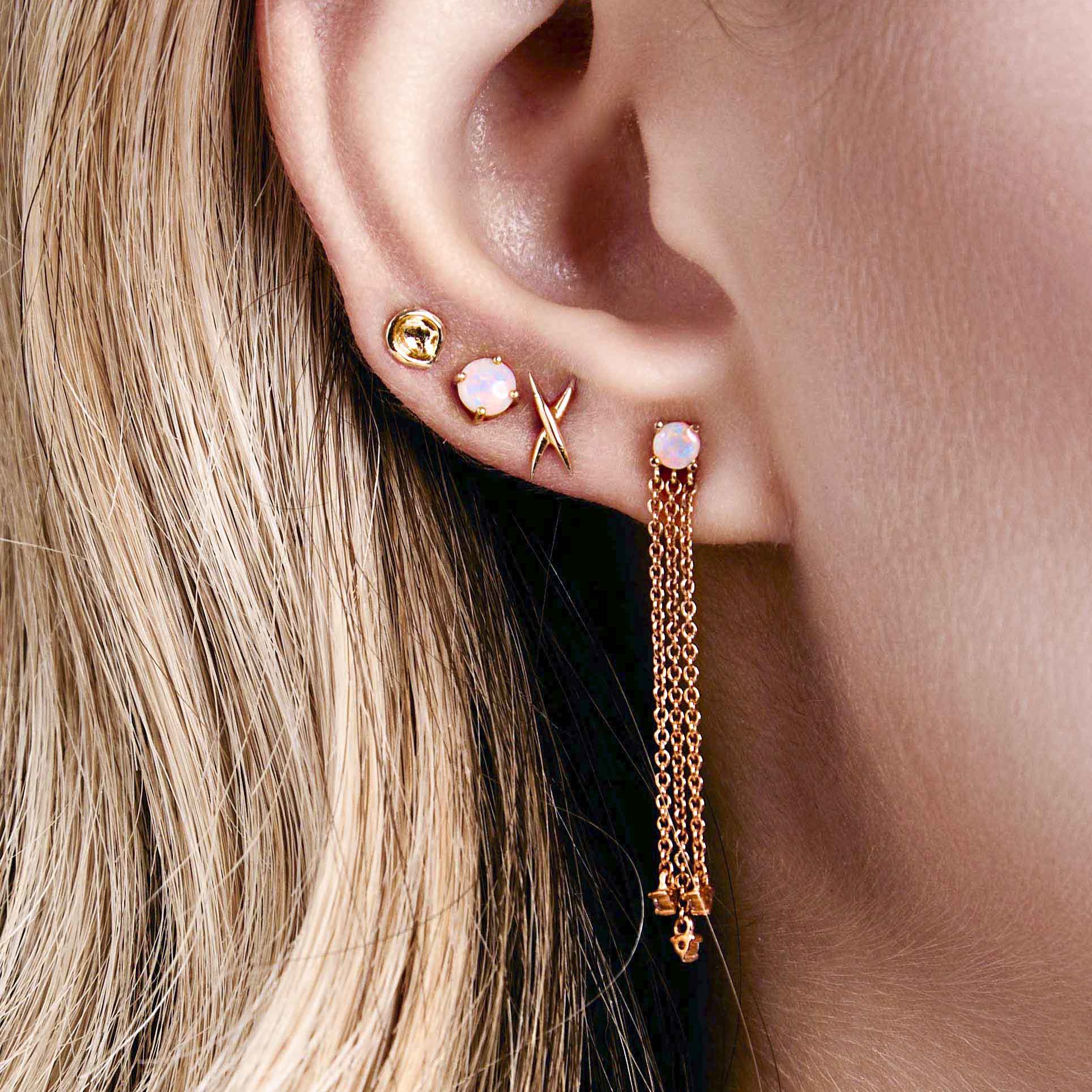 A pair of gold-colored stud earrings shaped like an X, australian opal studs on a ear. 