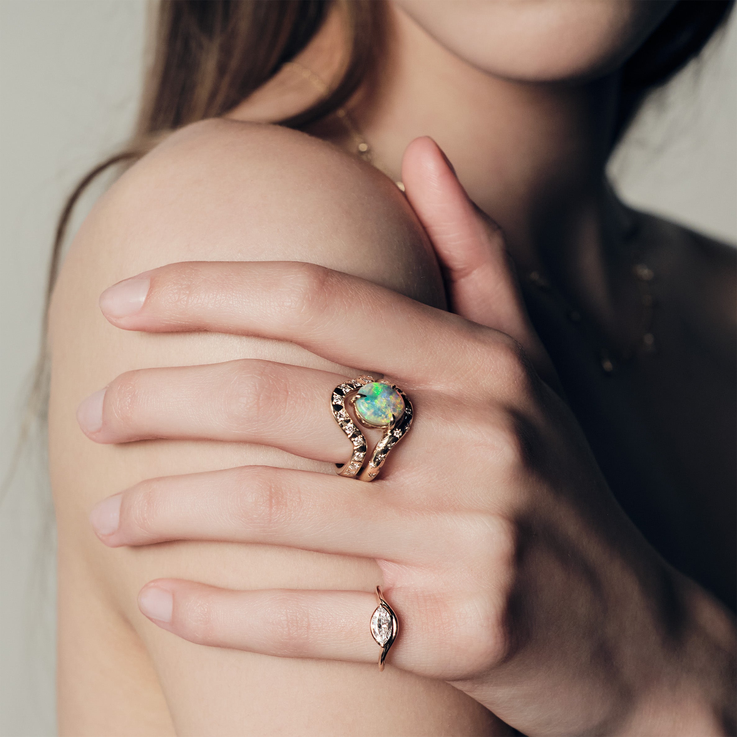 Close-up of a hand wearing a ring with a australian opal and diamonds, and a pinky ring with a marquise diamond set in a curvy band.