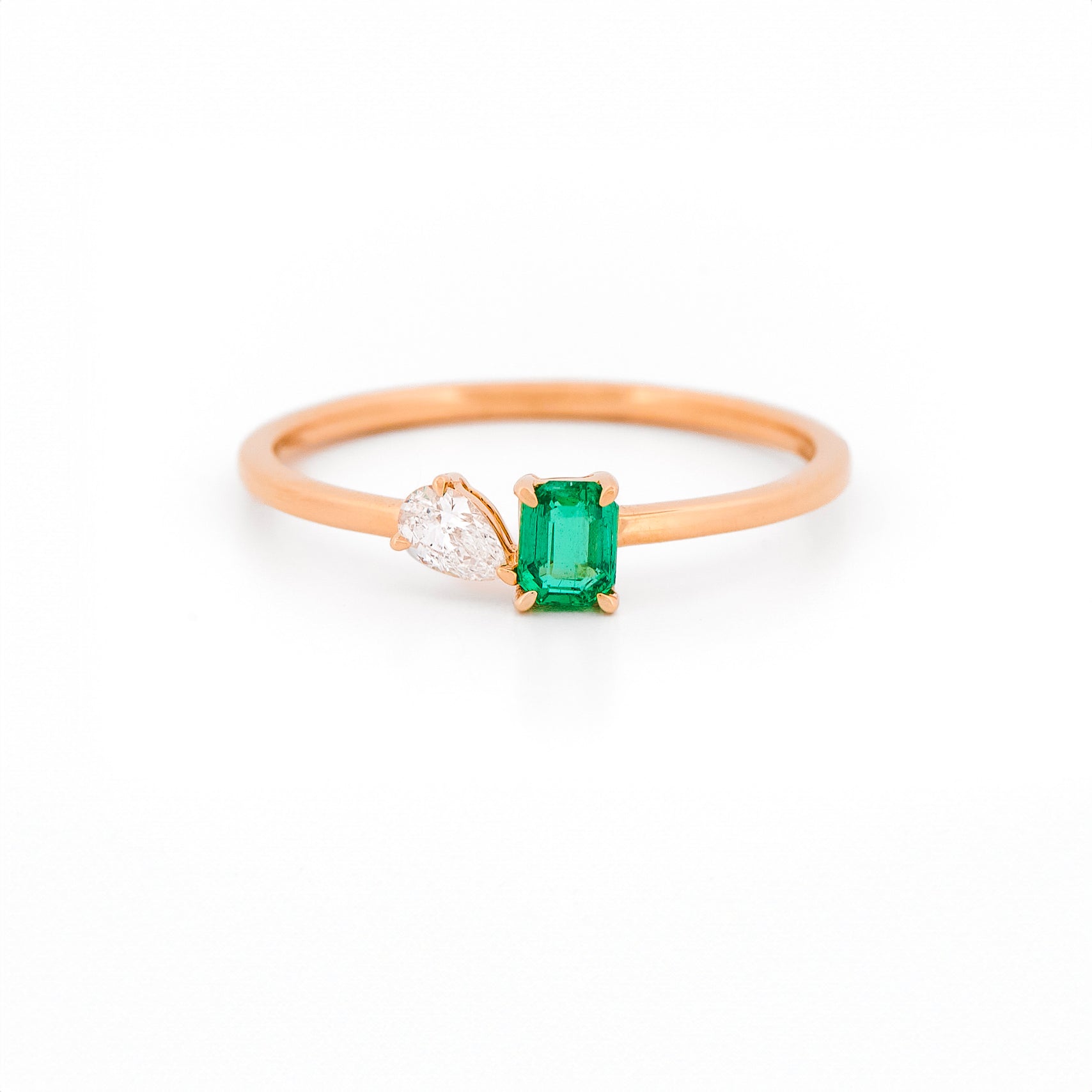 Rose gold toi et moi ring with an emerald and a diamonds on a white background