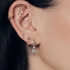 Close-up of an ear with The Chandelier Stud, Bubble Time 13mm Hoops, Floating Kite Diamond Stud, The Wild Rose Ruby Stud, Tiny Dew Drops Australian Opal Hoops, focusing on jewelry details.