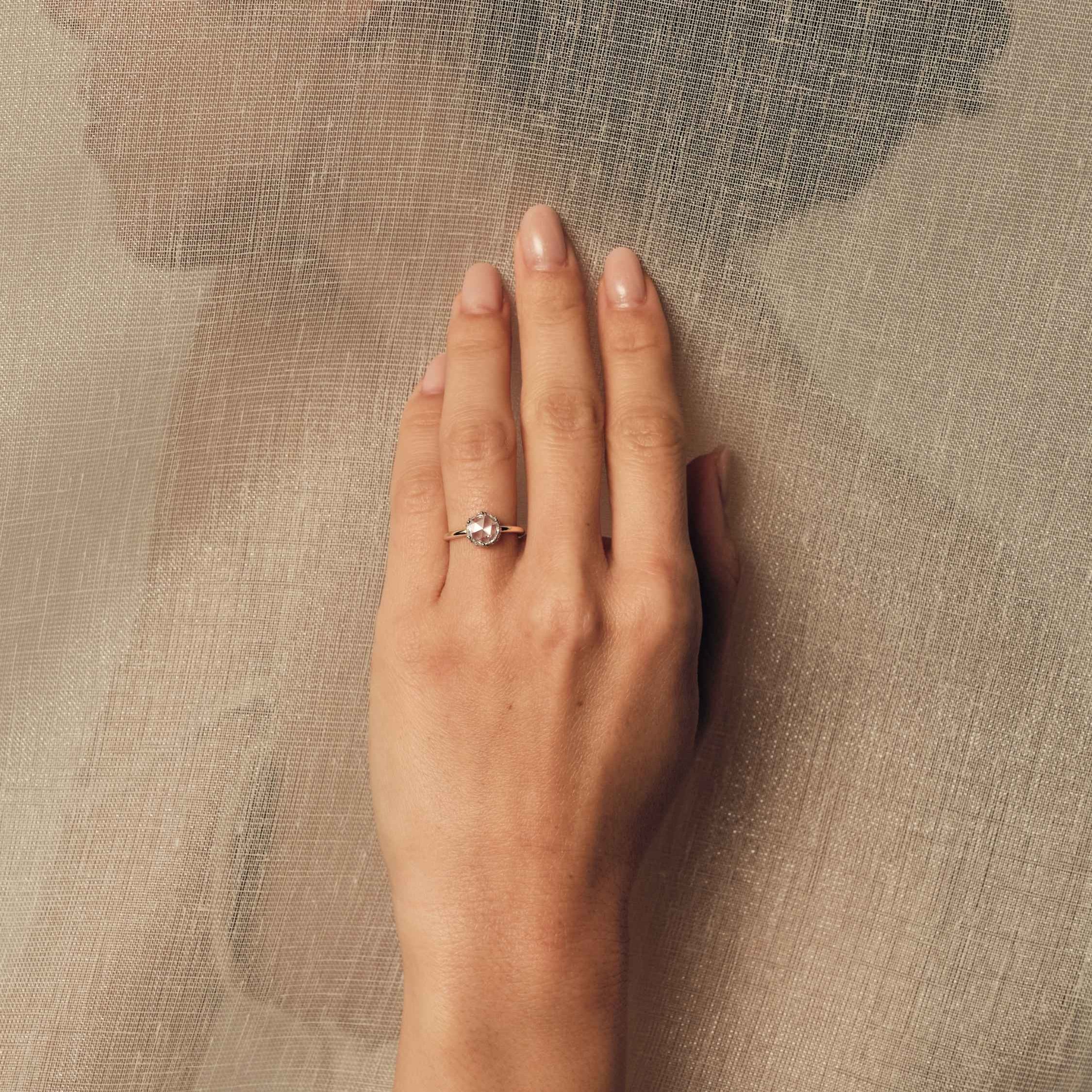 Hand wearing a rose cut diamond ring on a textured beige background.