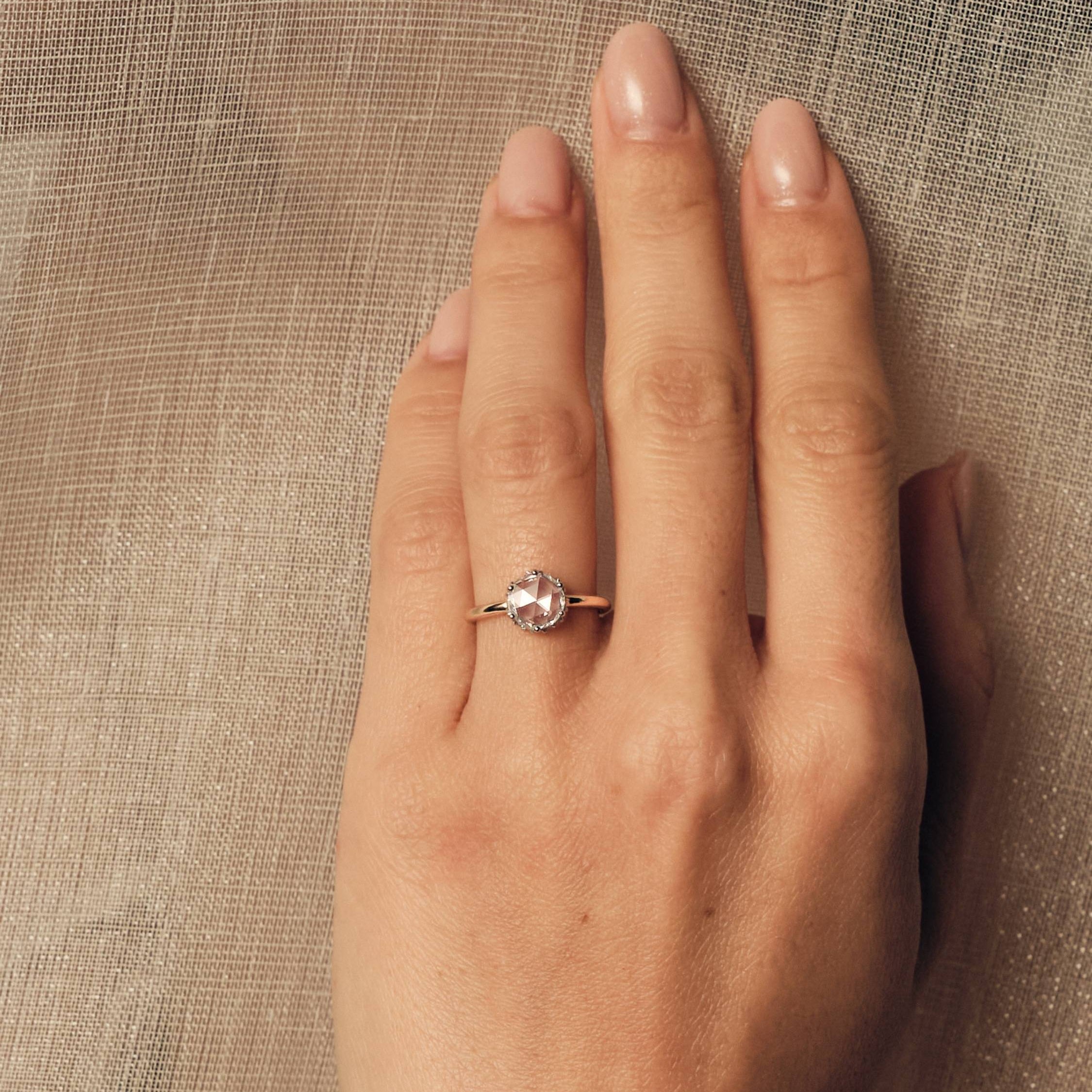 Hand wearing a rose cut diamond ring on a textured beige background.