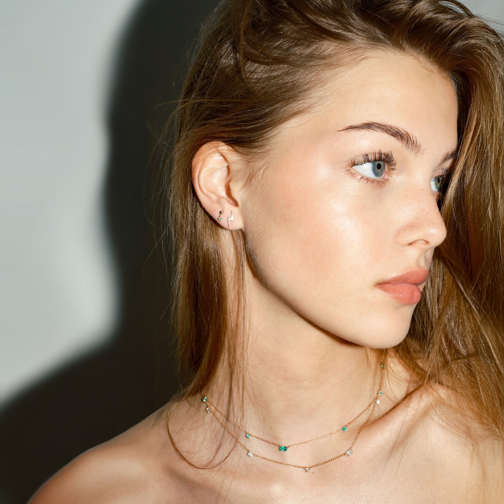 Close-up of a woman wearing delicate necklaces against a neutral background