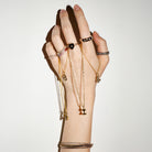 Hand wearing multiple gold bracelets and rings on a plain background