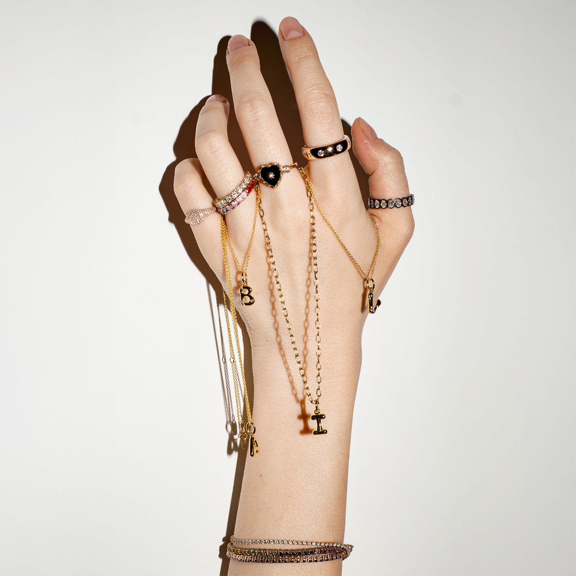 Hand wearing multiple gold bracelets and rings on a plain background