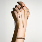 Hand wearing multiple pieces of gold  jewelry on a plain background
