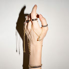 Hand wearing multiple pieces of gold  jewelry on a plain background