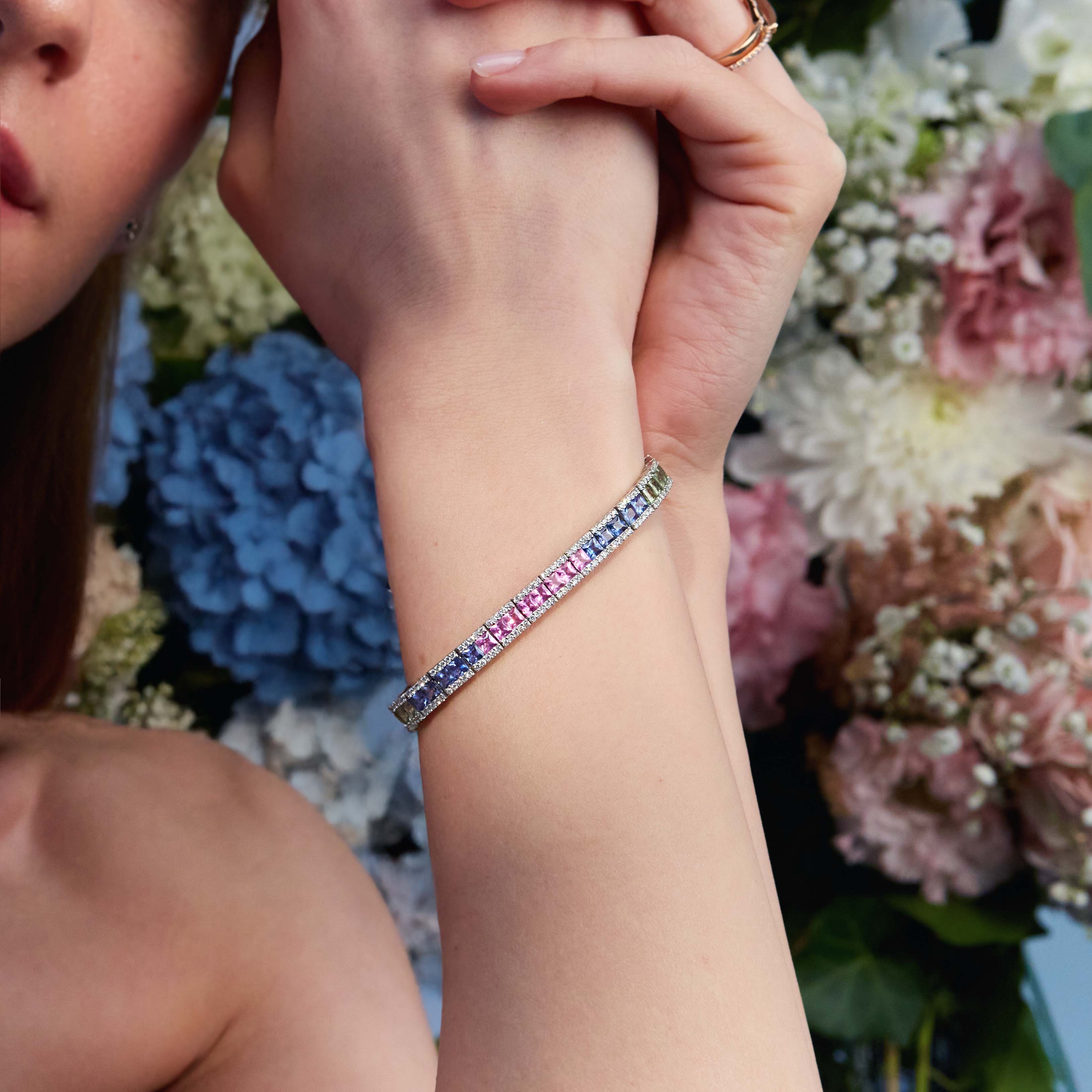 A woman wearing a tennis bracelet with rainbow sapphires and diamonds in 18k gold.