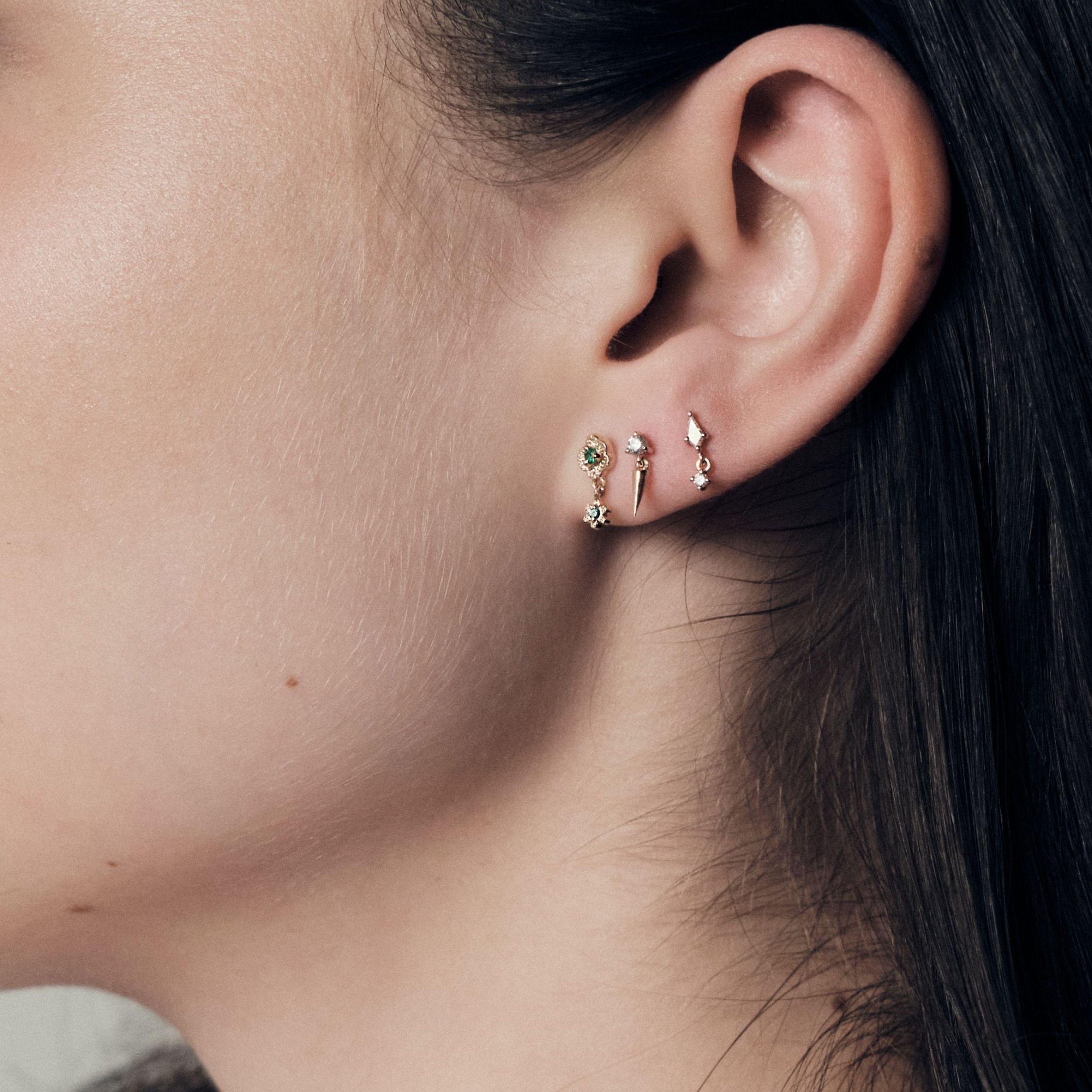 Close-up of an ear wearing a set of earrings, wild rose stud, gold icicle stud and floating kite stud.