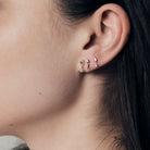 Close-up of an ear wearing a set of earrings, wild rose stud, gold icicle stud and floating kite stud.